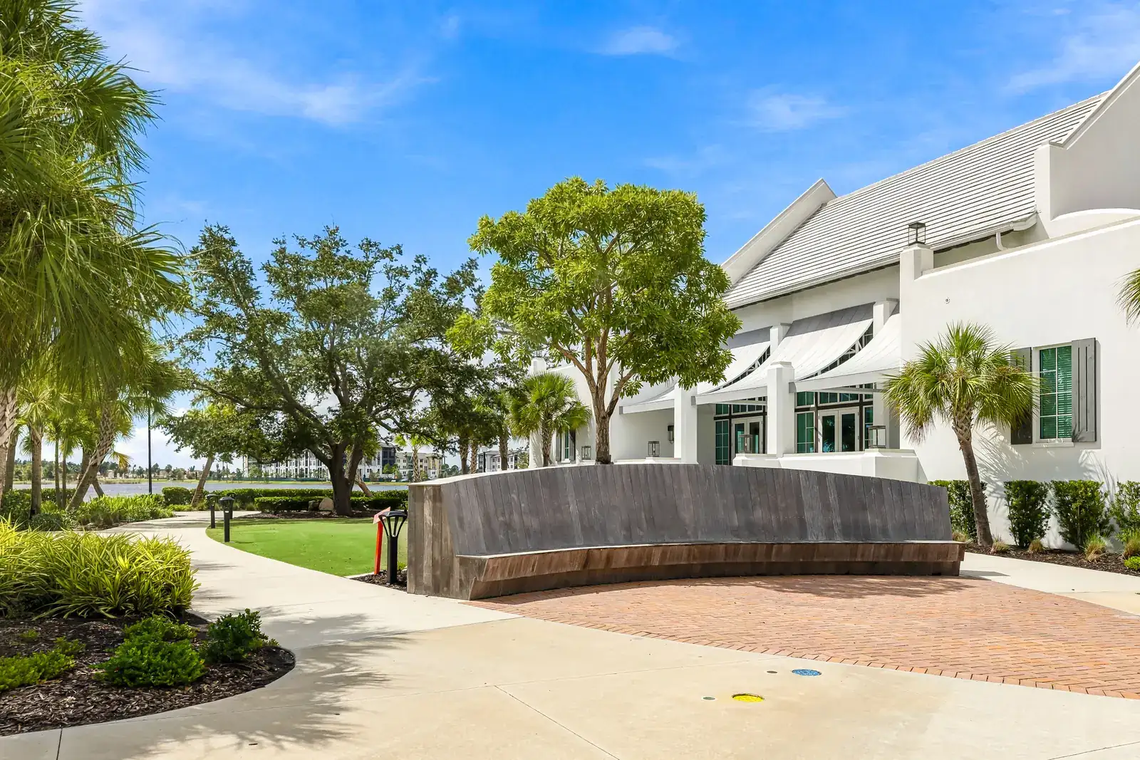 Curved seat wall and brick paving under live oaks beside a white lakefront building in Wellen Park